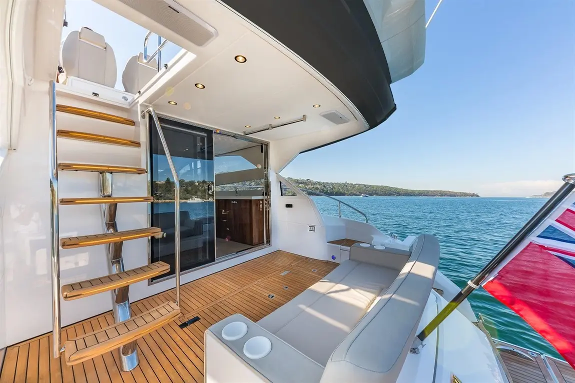 Stylish yacht deck featuring wooden steps, a spacious seating area, and panoramic views of the water and coastline.